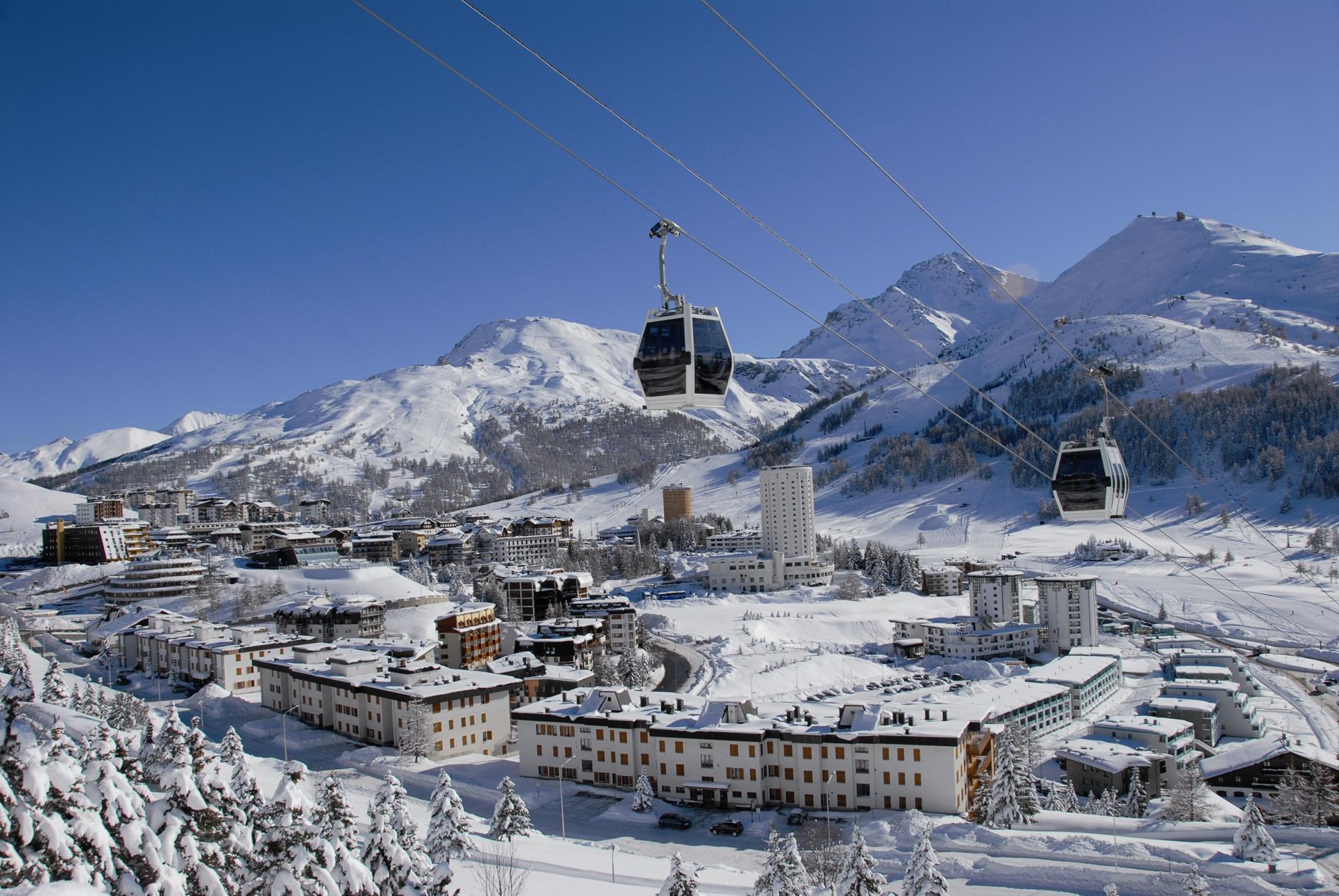Gondolas tranporting skiiers up mountain with town of sestriere